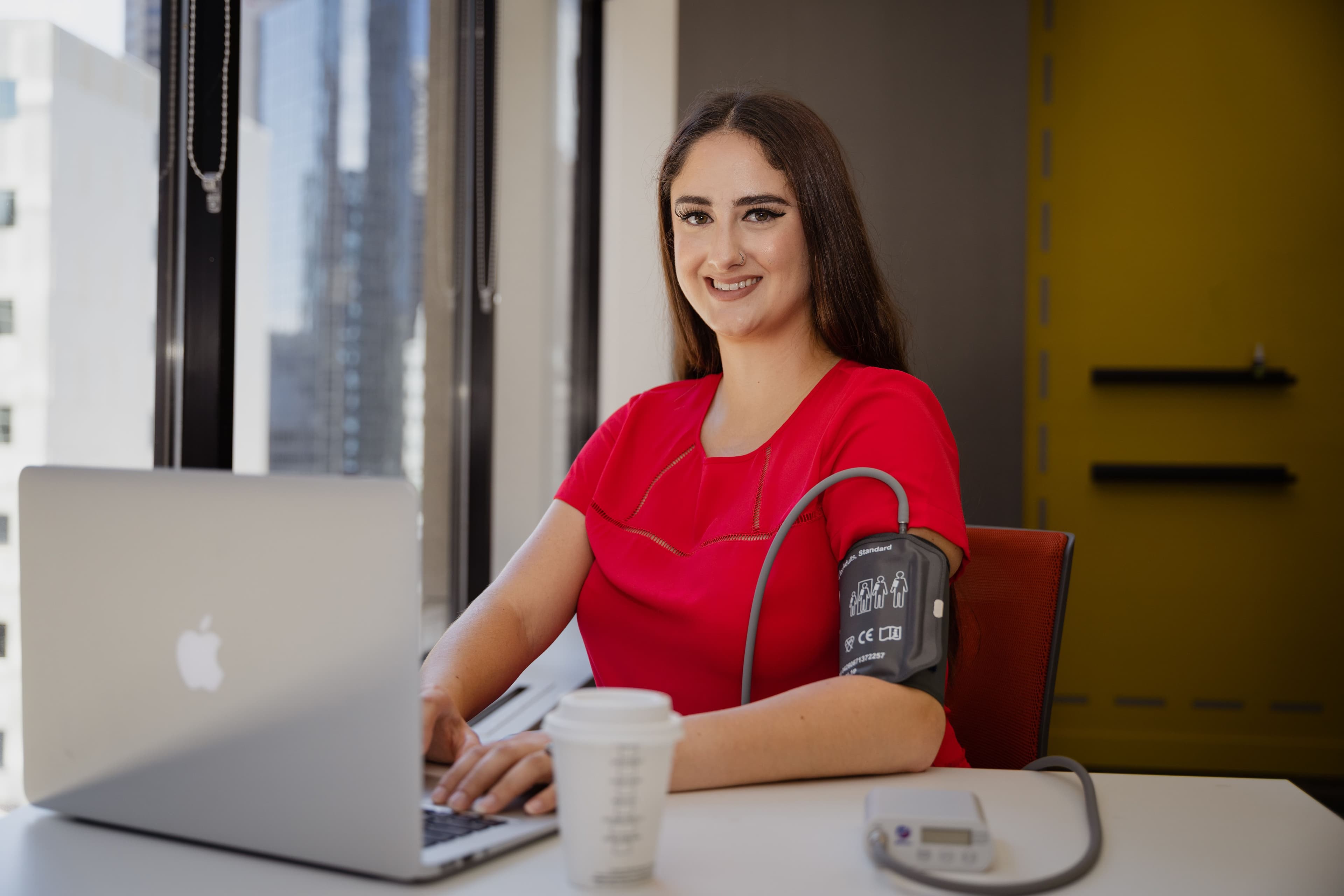 A community participant checking her blood pressure with the BPAro device while working on her laptop